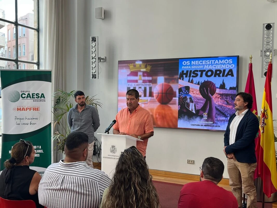 Público asistente al acto de presentación con la pantalla 'OS NECESITAMOS HACIENDO HISTORIA' al fondo